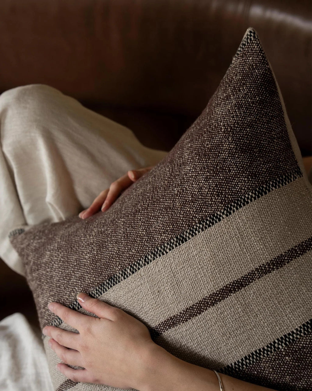 Weave Home Ottavio cushion in Mulberry styled on a leather sofa.