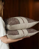 Two Weave Home Ottavio cushions in Mulberry, carried against a wood-panelled wall.