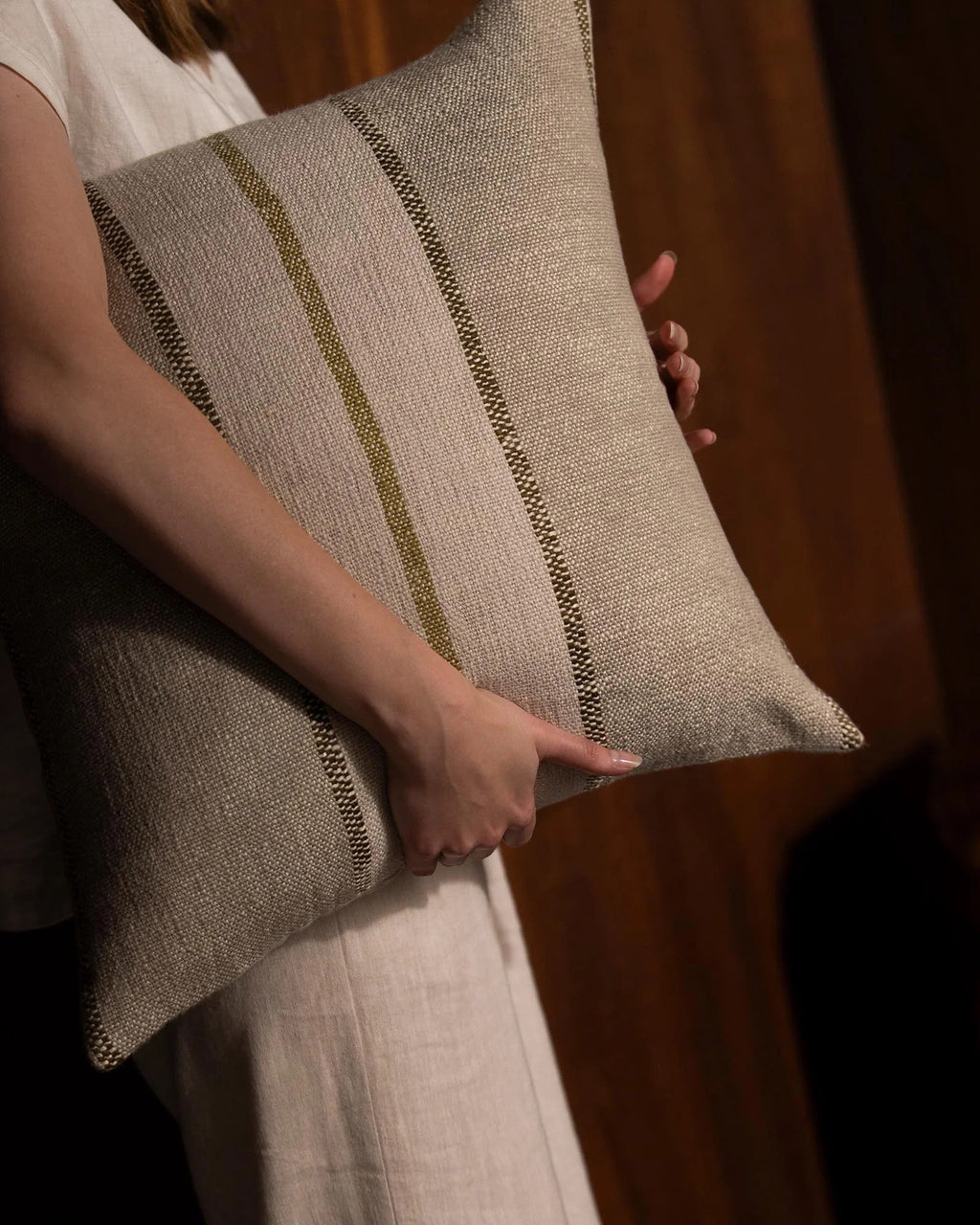 Weave Home Ottavio cushion in Willow held close, with a second cushion beside it and a wood-panelled background.