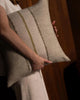 Weave Home Ottavio cushion in Willow held close, with a second cushion beside it and a wood-panelled background.