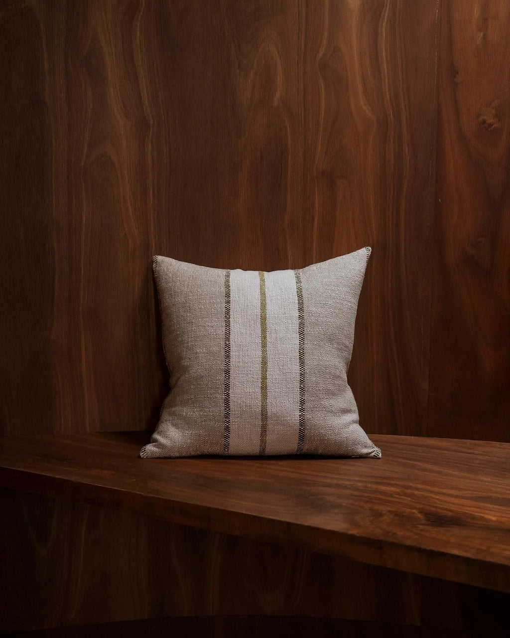 Weave Home Ottavio cushion in Willow on a walnut bench, against a walnut-panelled wall.