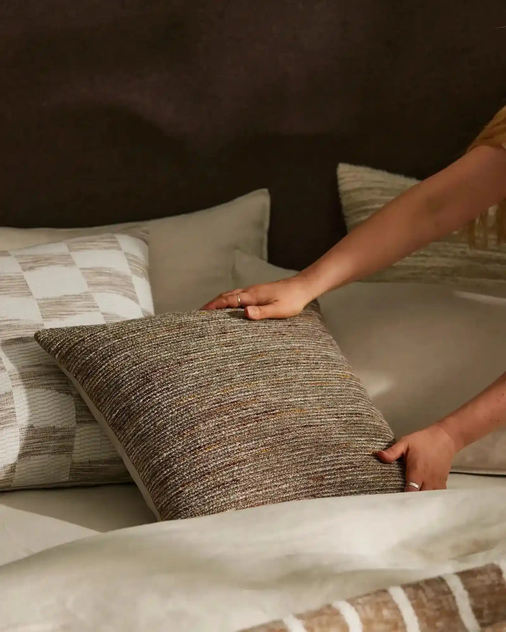The Weave Home brown-toned 'Vista Natural' cushion being placed on a bed 