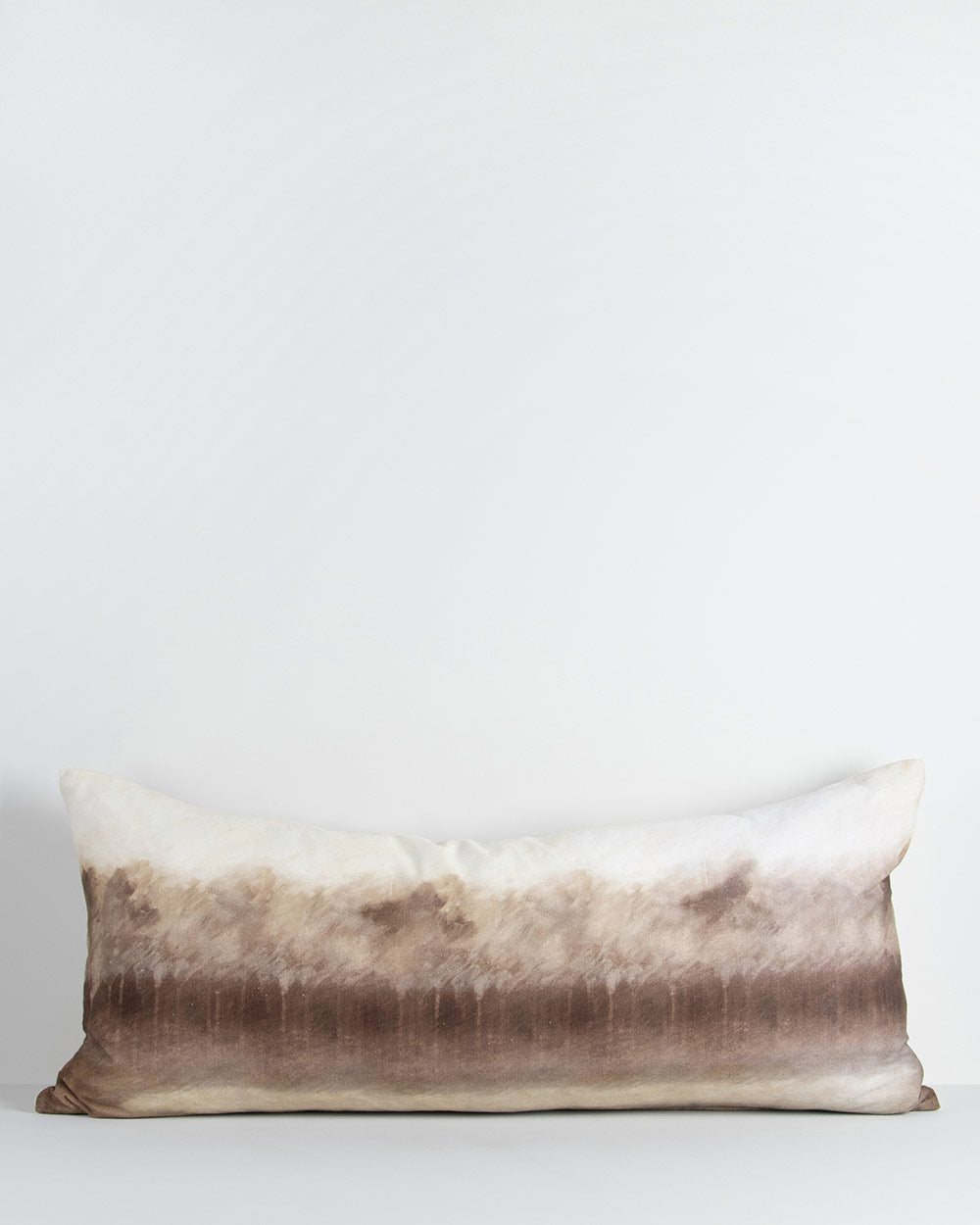 A long lumbar cushion with a watercolour painting of abstract forest trees in shades of sienna and umber printed onto it. By Baya