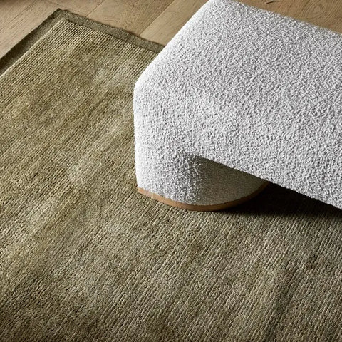A 100% wool floor rug in moss green colour, seen under a bench seat in a modern living room