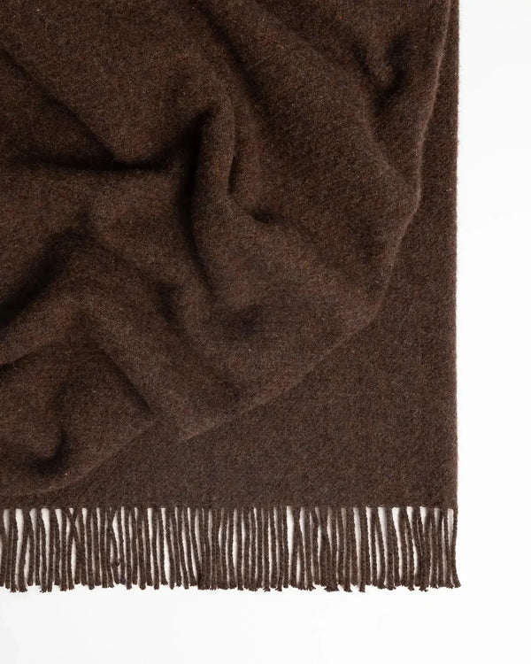 A rich, chocolate brown recycled wool throw blanket with fringe