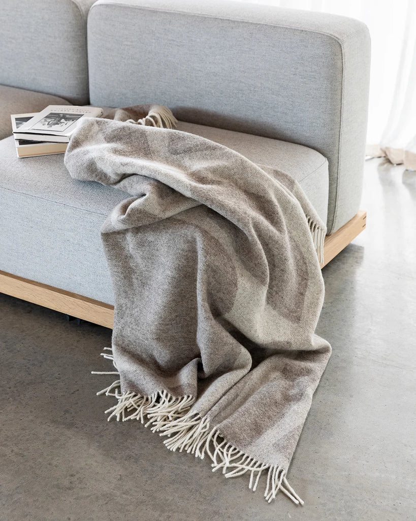 Baya 'Flagstone' NZ wool throw blanket in beige brown tones, draped on a couch in a stylish  home