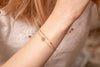 A woman wearing a delicate gold chain link bracelet with a grey-green labradorite crystal in the centre. 