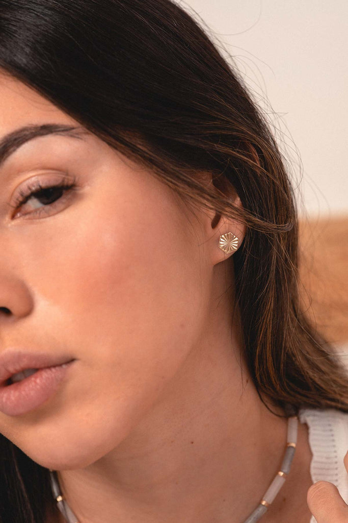 A woman wearing gold stud earrings, in a hexagon shape with a starburst pattern, by French designer Zoaje. 