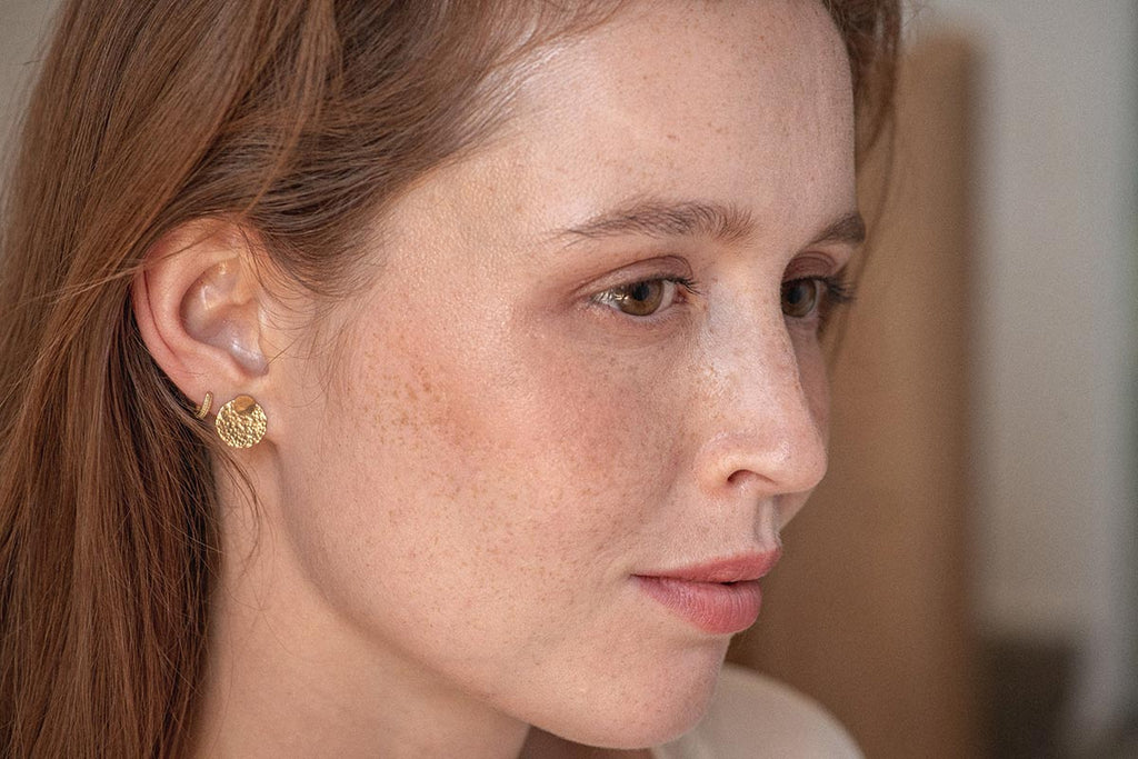 A woman wearing the beautiful Ecuador hammered yellow gold-fill stud earrings. 