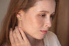 A woman wearing round stud earrings. The hammered jacket of the stud sits in front of her earlobe, catching the light. 