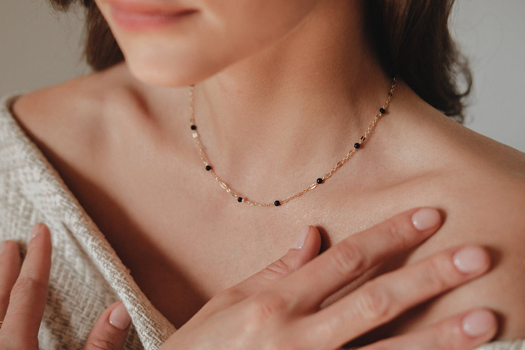 A woman wearing a delicate chain link necklace, interspersed with black agate beads. 