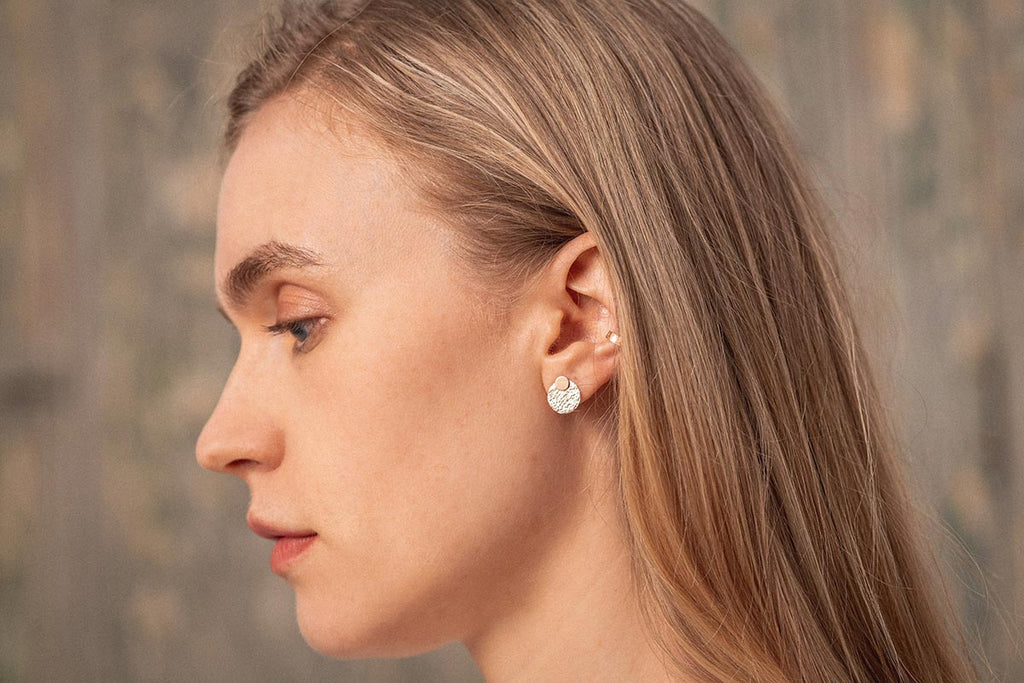 A profile view of a woman wearing textural yellow-gold earrings, that catch the light.