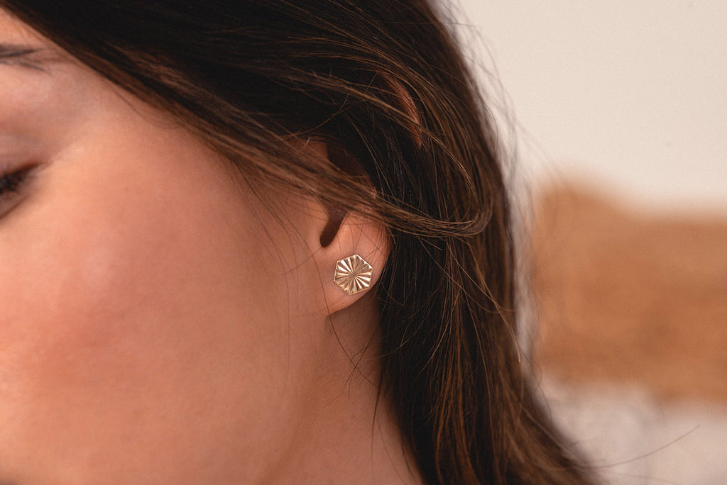 A woman wearing the Zoaje stud earrings. They sit beautifully on her earlobe, the starburst pattern catching the light. 