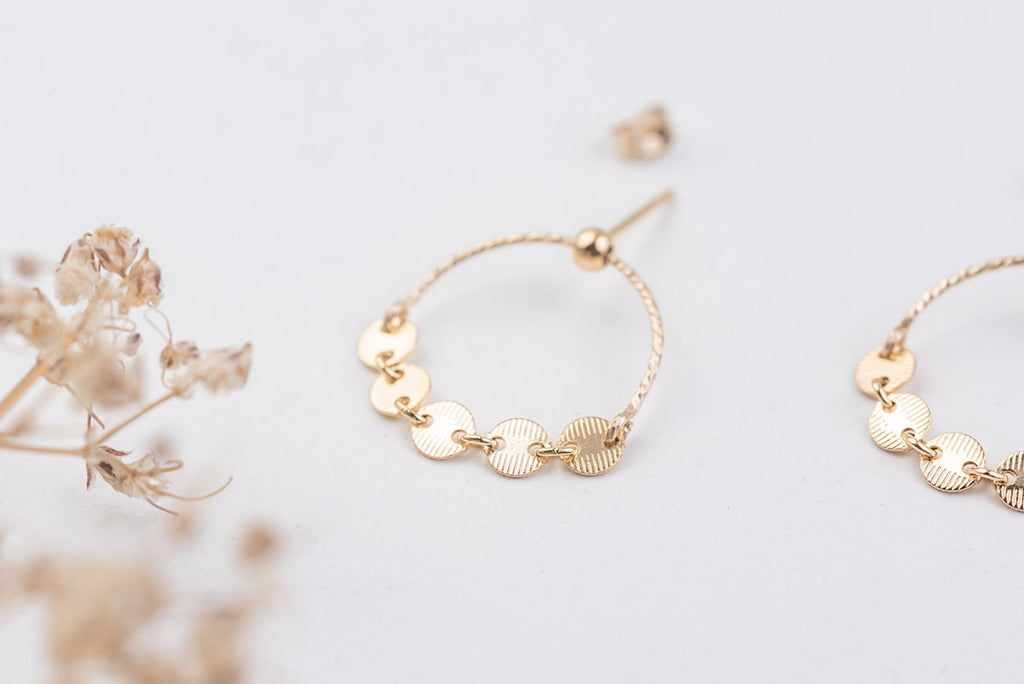 A close up view of two gold hoop earrings with stud backs, with five gorgeous tiny brushed metal discs as charms at the centre. 
