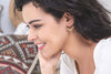 A smiling woman sits in profile to the camera, giving us a great look at her delicate earrings, made with yellow gold by Zoaje. 