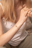 A woman wearing a delicate chain link bracelet in yellow gold-fill, with two strands. One of the strands is thinner than the other, and has a gorgeous labradorite charm on it. 