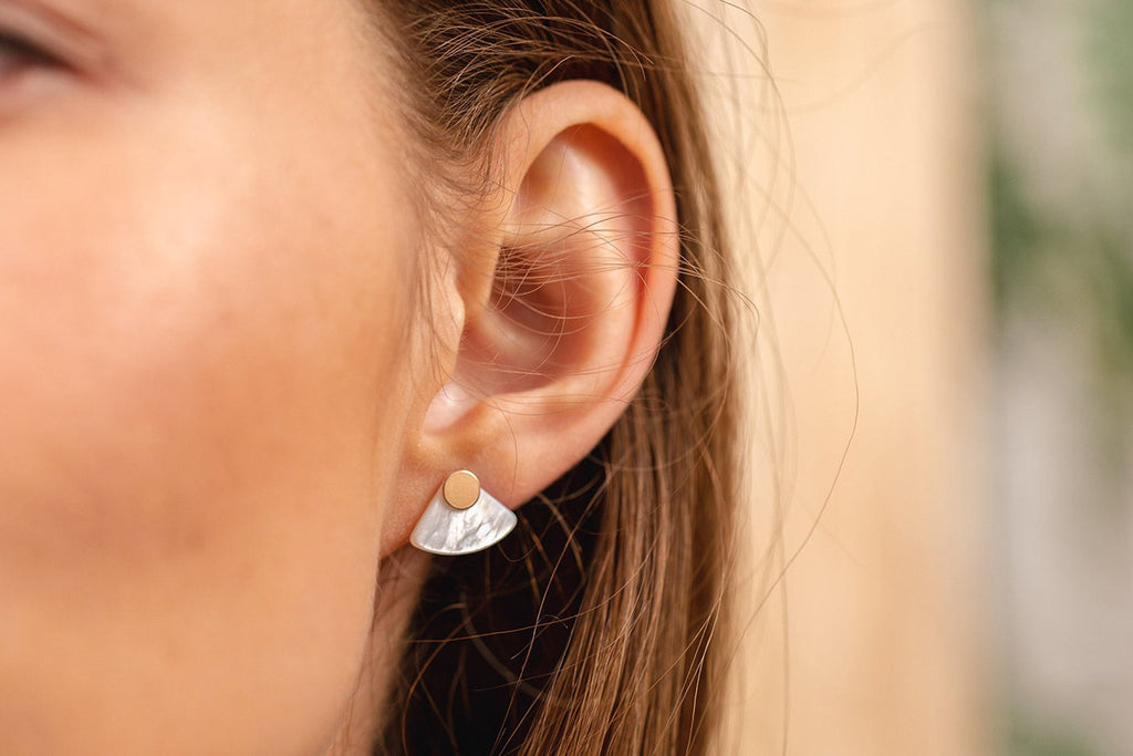 A woman wearing gold-fill and mother-of-pearl geometric stud earrings. 