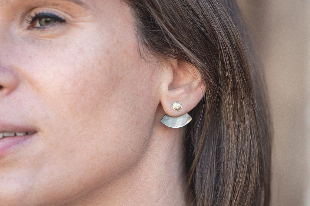 A woman wearing the Laos earrings in one of three ways. The Mother-of-pearl jacket is tucked behind her ear, highlighting the gold centre of the earring. 