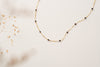 A gold filled chain link necklace with small beads of black agate on a white background