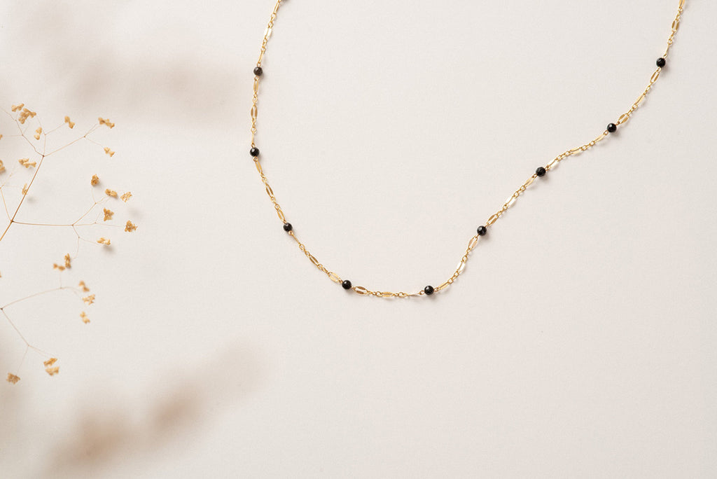 A gold filled chain link necklace with small beads of black agate on a white background
