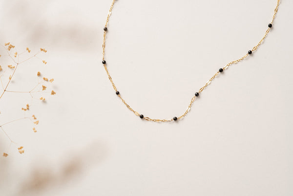 A gold filled chain link necklace with small beads of black agate on a white background