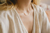 A woman's neck displaying a light-catching yellow-gold necklace with a fine, delicate chain. By Zoaje