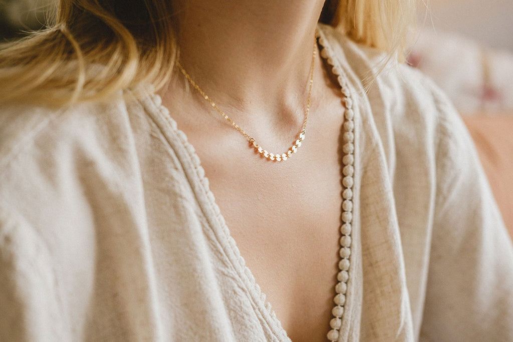 A woman's neck displaying a light-catching yellow-gold necklace with a fine, delicate chain. By Zoaje