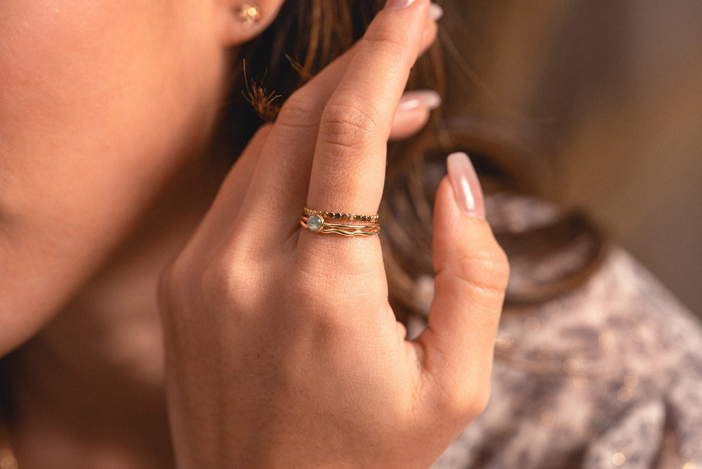 A woman wearing a delicate stack of three rings, with gold fill and a feature of natural labradorite