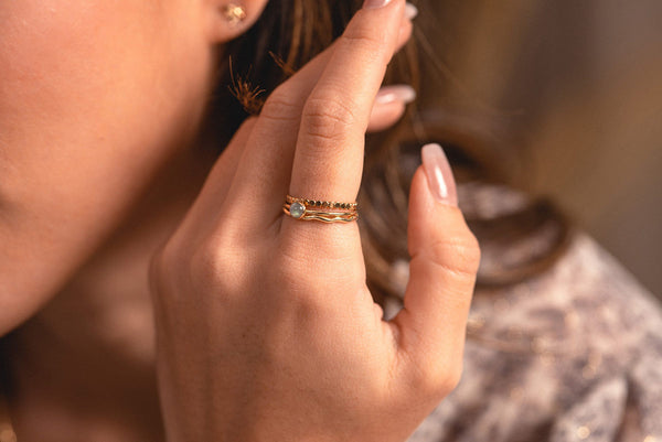 A woman wearing a delicate stack of three rings, with gold fill and a feature of natural labradorite