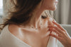 A stylish woman wearing a white cardigan and an intricate yellow gold necklace with black agate beads. 