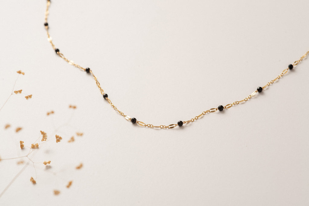 A delicate chain link necklace made with yellow gold, interspersed with black agate beads. 