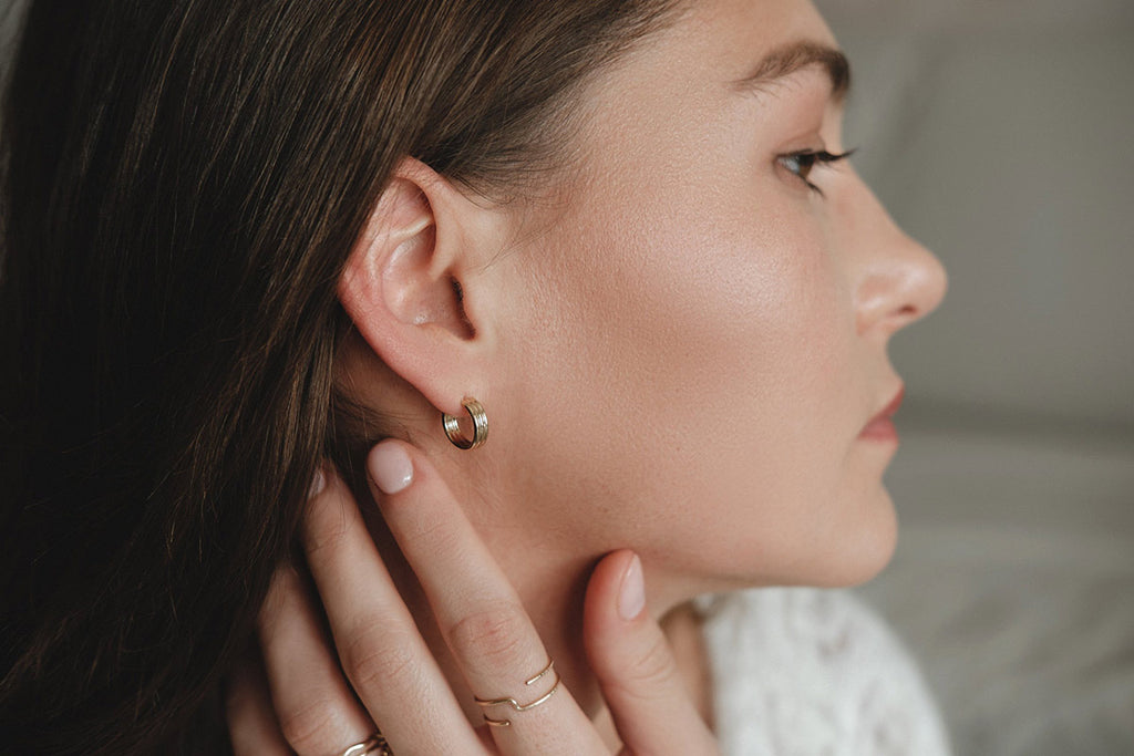 A woman wearing slightly thick, small, yellow gold hoop earrings by Zoaje. 