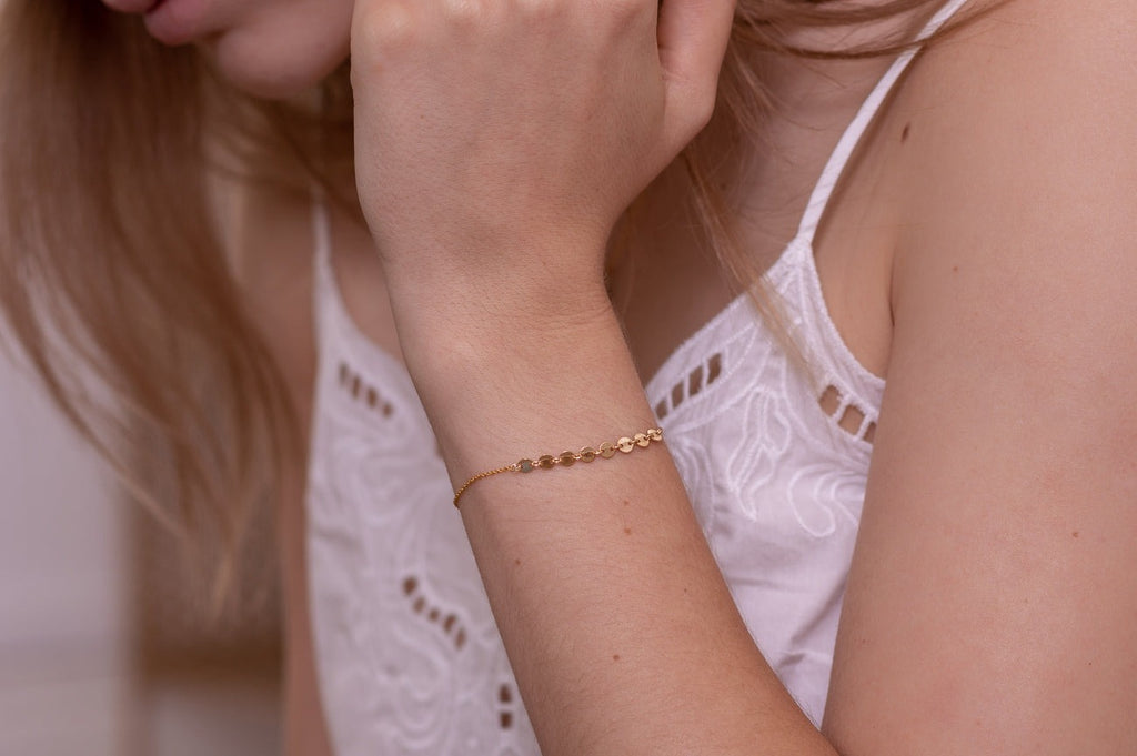 A woman wearing a delicate gold bracelet with circular hammered gold pieces. 