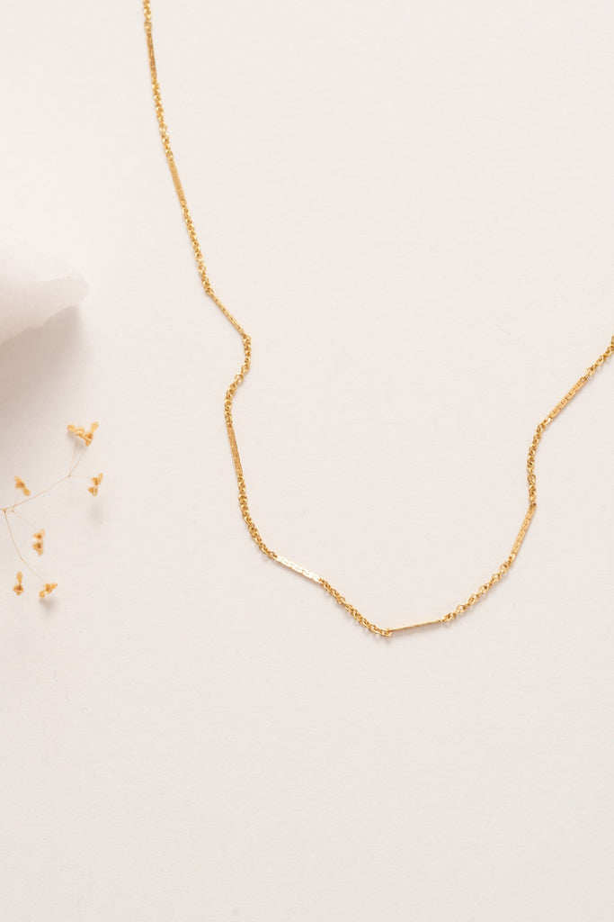 A fine delicate gold chain necklace with flattened sections giving texture. 
