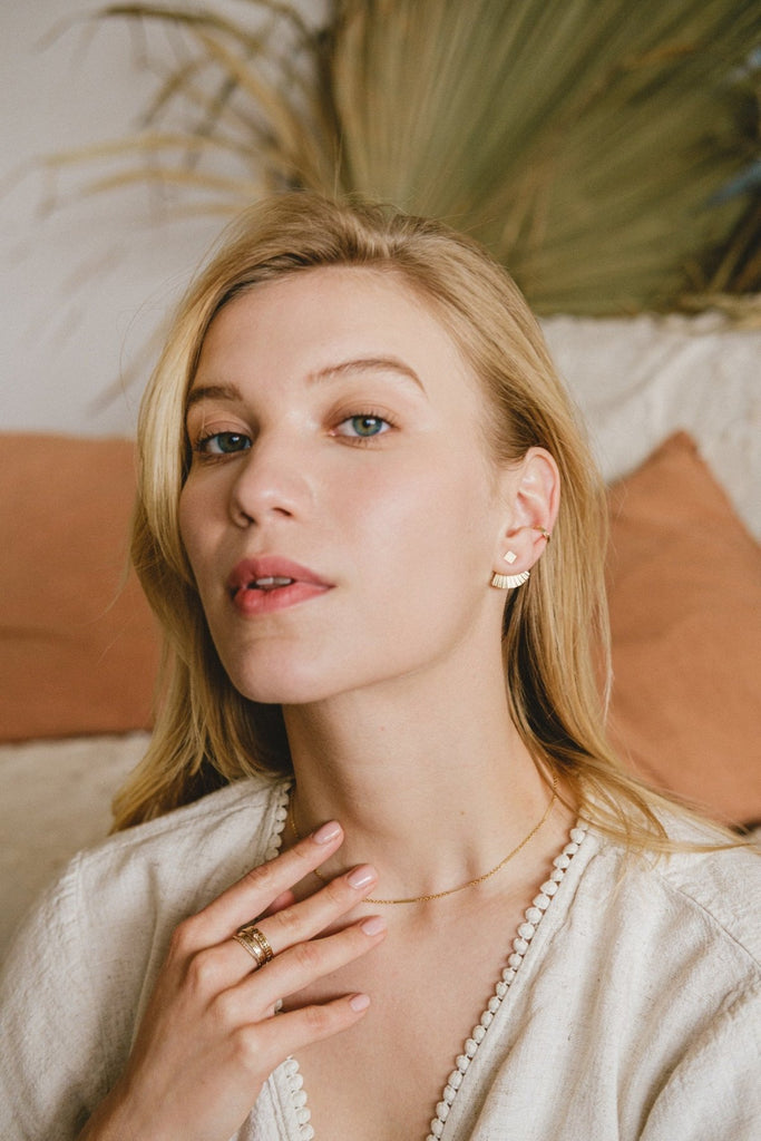 A woman wearing an assortment of delicate gold filled jewellery: necklace, rings, and earrings, by French Australian designers Zoaje. 