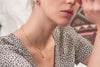A woman wearing two delicate gold filled necklaces by Zoaje - one is a simple chain with textured flattened sections, and one has a charm in the shape of a sand dollar. 