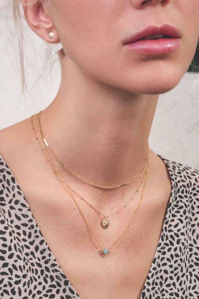 A woman wearing three necklaces in a stack: one plain with hammered chain sections, and two with delicate 14k gold-filled charms. 