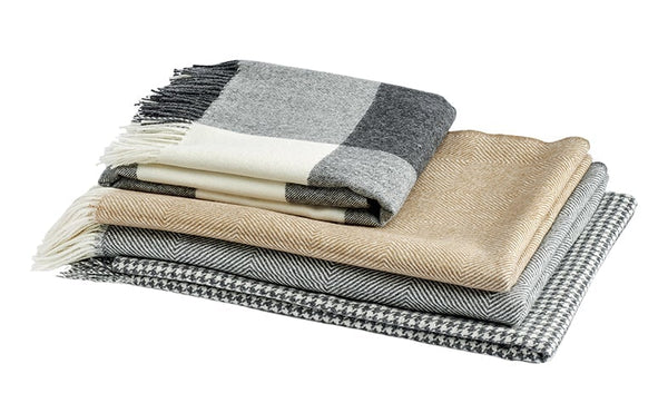A beautiful pile of luxurious Christian Fischbacher throws in soft alpaca yarn, folded and clean cut against white