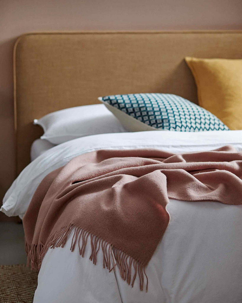 A stunning contemporary bedroom interior featuring a 100%  NZ lambswool throw in a dusky pink rose colour; by Weave Home NZ