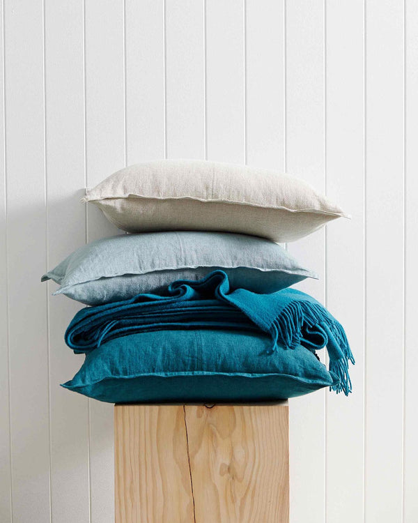A stack of linen cushions, and a turquoise lambswool throw, in beautiful blue hues by Weave Home NZ