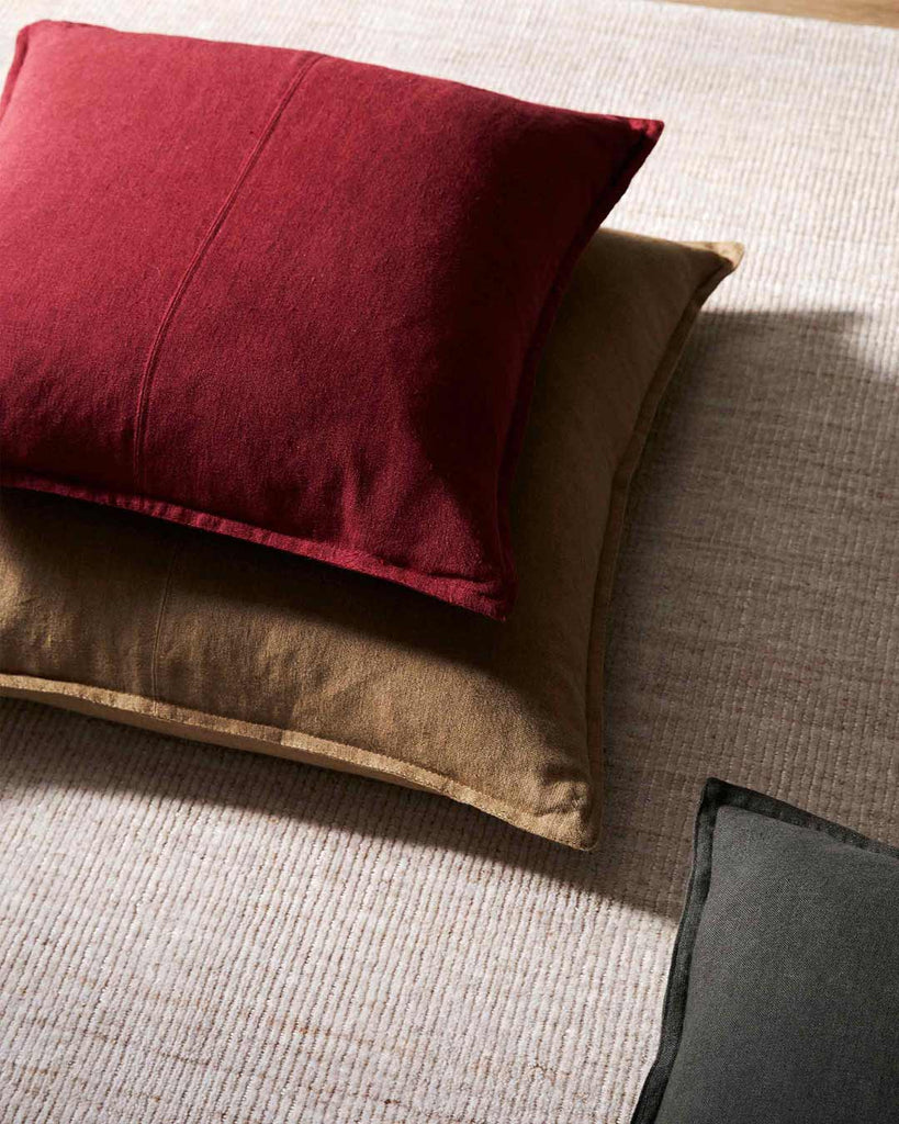Rhubarb Red Como Linen Cushion with panel detail, by Weave Home NZ,. Sitting on top of brown linen cushion on rug