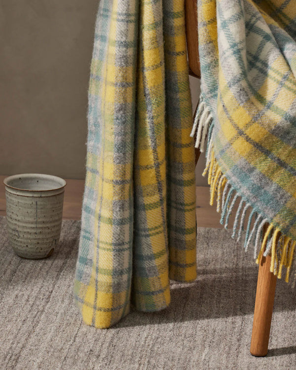 The Weave Home Brighton Butter wool throw draped over a chair, featuring a sunny yellow plaid design 