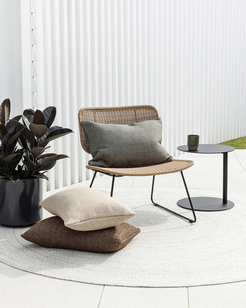 A cozy looking wicker chair with cushions by Baya NZ, sitting on a white outdoor rug, also by Baya NZ