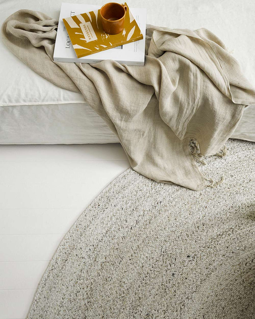 A cool white rug by Baya NZ depicted inside next to a couch, with a beige throw also by Baya NZ. 